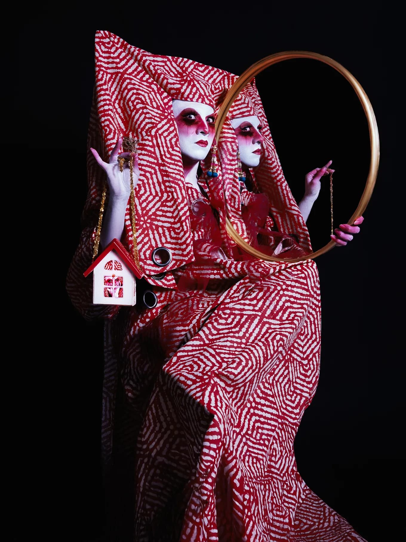 Vermelha con un vestido rojo y blanco sostiene un espejo dorado